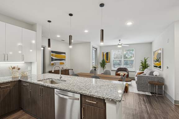 A modern kitchen with a granite countertop and a dining area with a grey sofa.