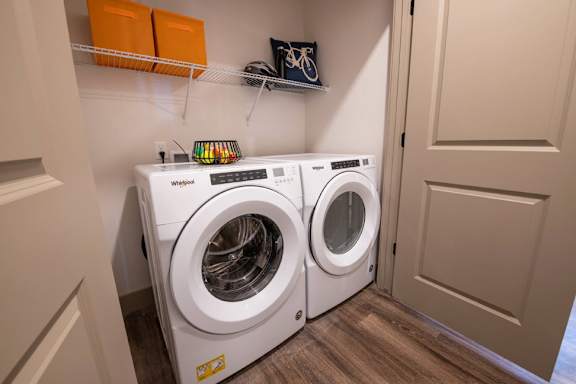 A pair of white front loading washing machines in a small laundry room.