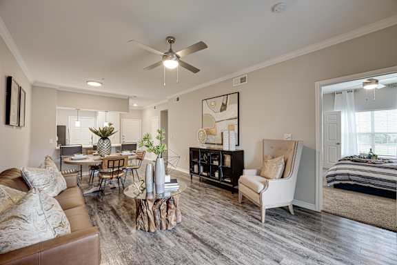 A living room with a brown leather couch, a wooden coffee table, a white armchair, and a black bookshelf at Highland Luxury Living Apartments in Lewisville, TX.