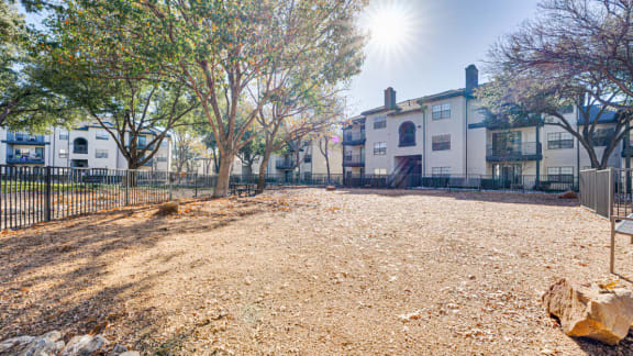 Dog park with gravel surface and mature trees at Carmel Creekside Apartments, Fort Worth, TX