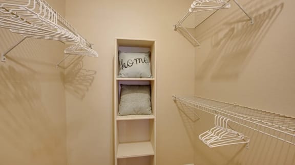 Large closet with shelves and a shelf with a pillow that says welcome at Indian Creek Apartments in Carrollton, TX