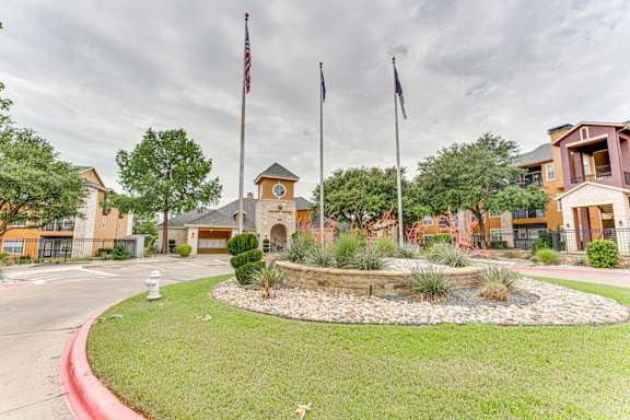 Property entrance with flagpoles and landscaped courtyard at Limestone Ranch Apartments, Lewisville, TX