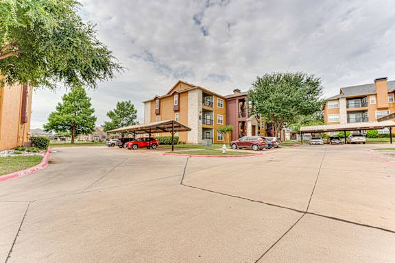 Parking area with covered carports and apartment buildings at Limestone Ranch Apartments, Lewisville, TX