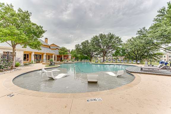 Swimming pool with tanning ledge and white loungers at Limestone Ranch Apartments, Lewisville