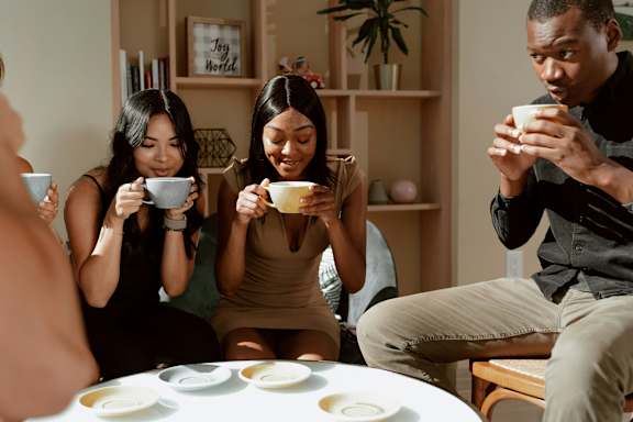Three people are sitting around a table, each holding a cup and looking at a plate of food in front of them.