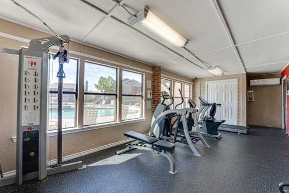 Fitness center with strength training equipment and pool view at Towne Centre Village Apartments, Mesquite
