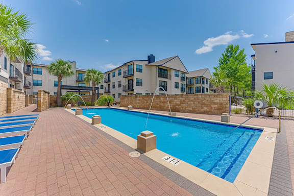 Pool with lounge chairs and brick paver deck at Vue Live Oak Apartments, Texas