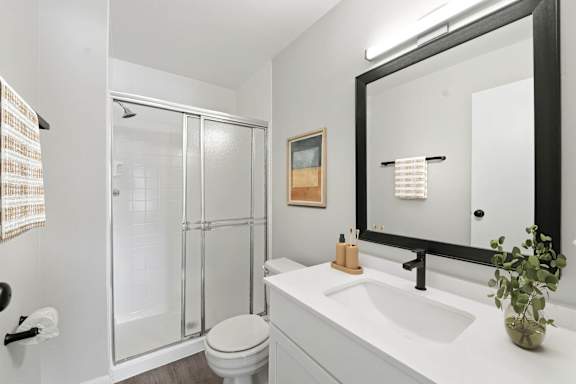 A bathroom with a white sink, toilet, and a glass shower stall.