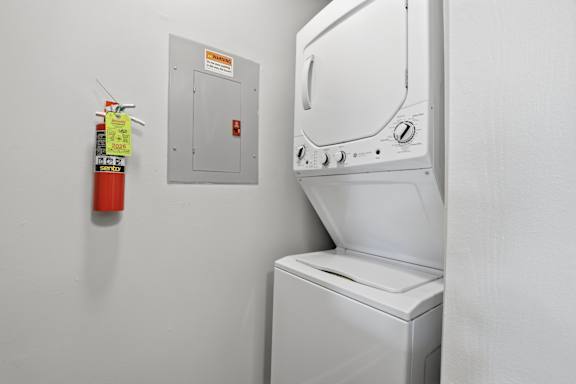 A white washing machine sits next to a fire extinguisher in a laundry room.