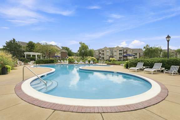 A large outdoor swimming pool surrounded by lounge chairs and a residential area in the background.