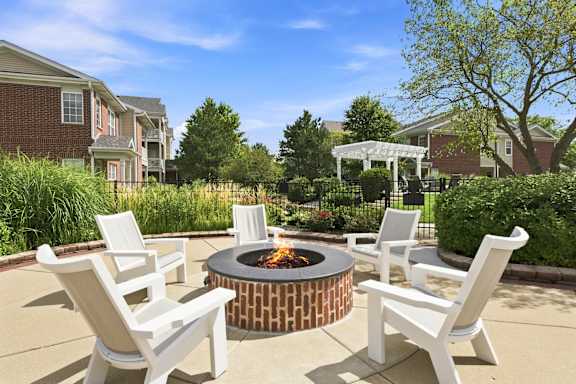 A fire pit surrounded by white chairs in a backyard.