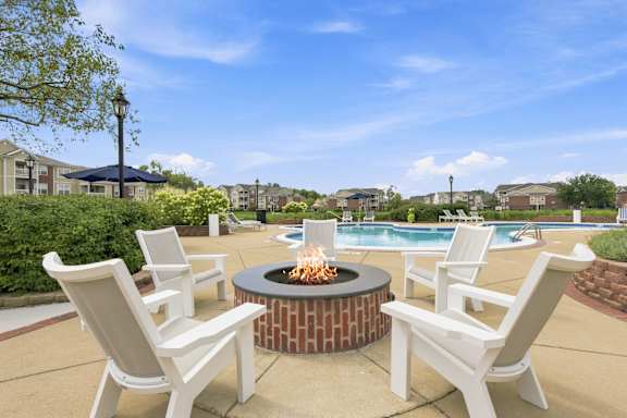 A fire pit sits in the middle of a patio surrounded by chairs.