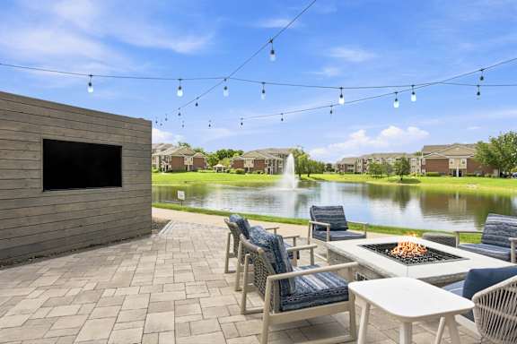 A patio with chairs and a table is set up with a lake and houses in the background.