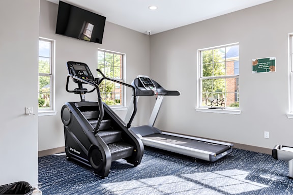 A black treadmill and a black exercise bike in a room with a window.