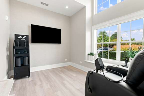 A black leather chair is in front of a flat screen TV in a room with a large window.