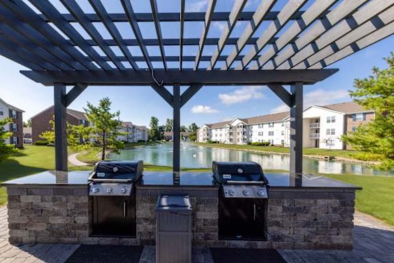 A grill and trash can are under a pergola.