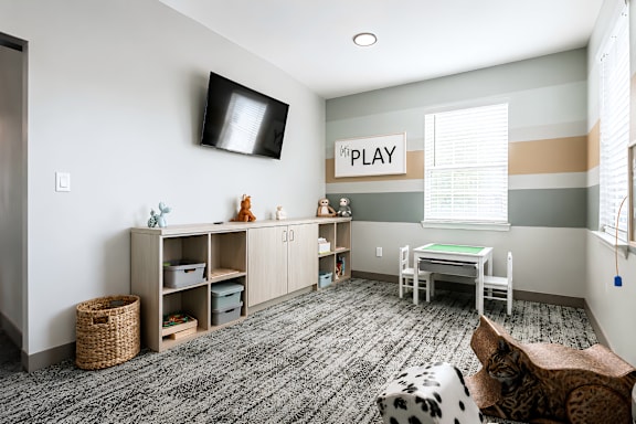 A room with a grey carpet and a sign that says "PLAY" on the wall.