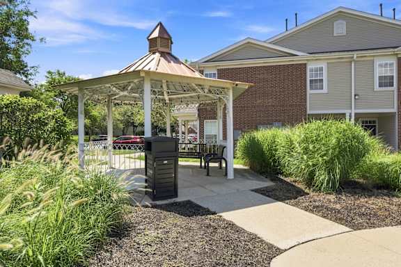 A gazebo is surrounded by plants and a building is in the background.