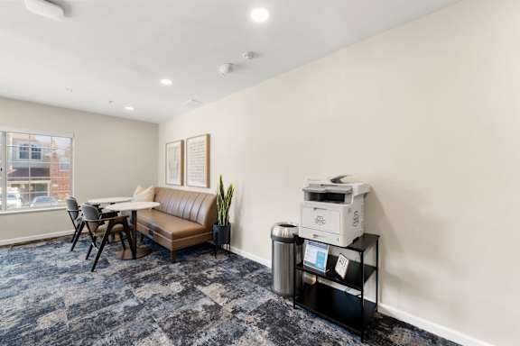 A room with a couch, a printer, and a trash can.
