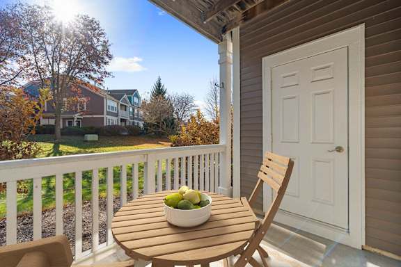 A table with a bowl of fruit on it sits on a porch.