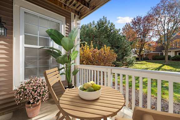 A wooden chair sits on a porch with a bowl of fruit on the table.