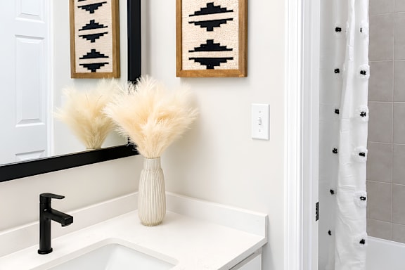 A white sink with a black faucet and a vase with white flowers.
