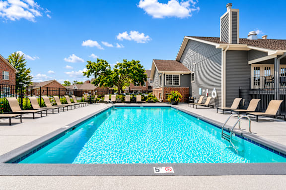 A swimming pool in front of a house with a poolside lounge.