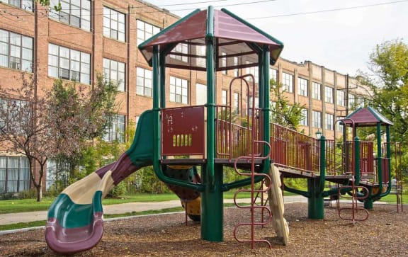 a playground with a slide in front of a large brick building