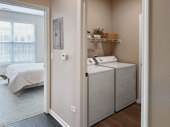 A small bedroom with a bed, laundry basket, and washing machine.
