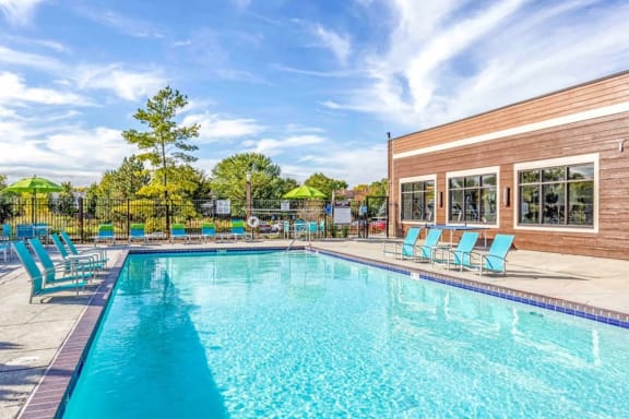 a swimming pool with blue chaise lounge chairs and a brick building with windows