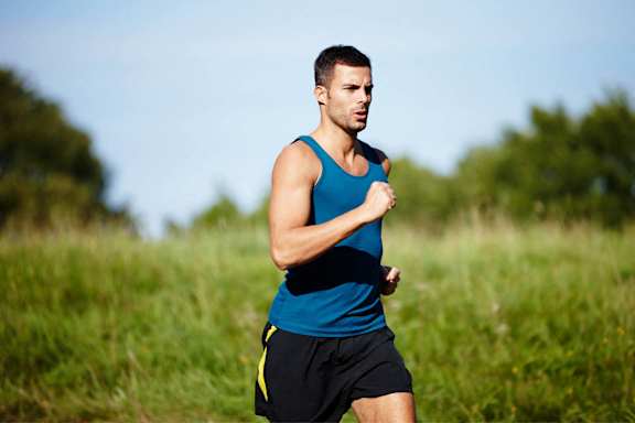 A man in a blue top and black shorts is running in a field.