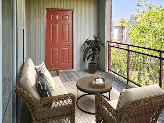 A balcony with a red door, a wicker chair, and a small table.