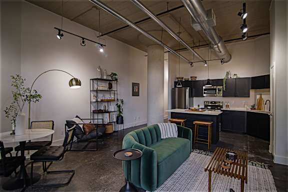 A living room with a green couch and a kitchen in the background.