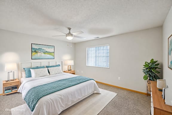 A bedroom with a bed, a ceiling fan, and a painting on the wall.