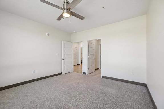 Bedroom with neutral carpeting, ceiling fan, and separate doorways connecting to the hall and adjoining space.