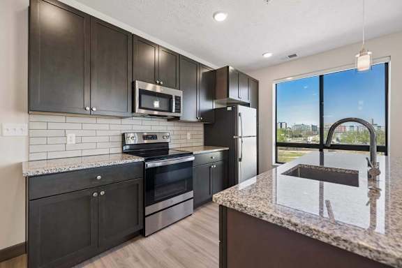 Modern kitchen with dark cabinetry, granite countertops, stainless steel appliances, and a large island overlooking city views.