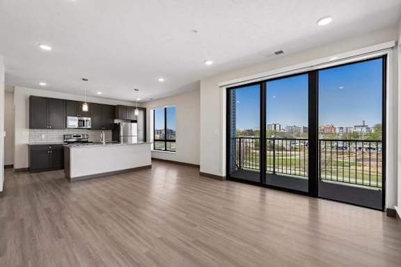 Spacious open-concept living room and kitchen framed by floor-to-ceiling windows and balcony access.