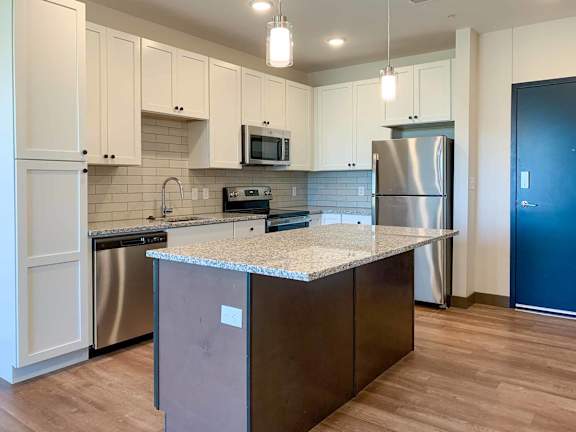 a kitchen with stainless steel appliances, light cabinets, and granite counter tops