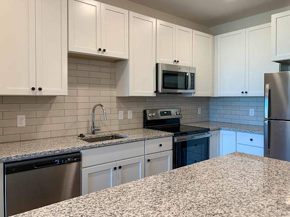 a kitchen with granite counter tops, stainless steel appliances, and white cabinets