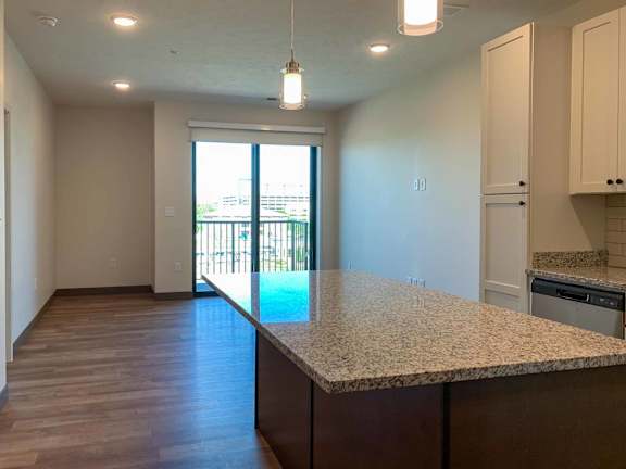 a kitchen with an island with a granite counter top and a living room with a door to a balcony