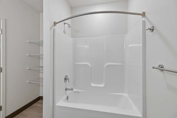 Apartment bathroom with a tub-shower combination, curved curtain rod, built-in shower shelves, and adjacent open storage shelving.