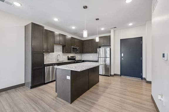 Modern apartment kitchen with dark cabinetry, granite island, stainless steel appliances, subway tile backsplash, and pendant lighting.