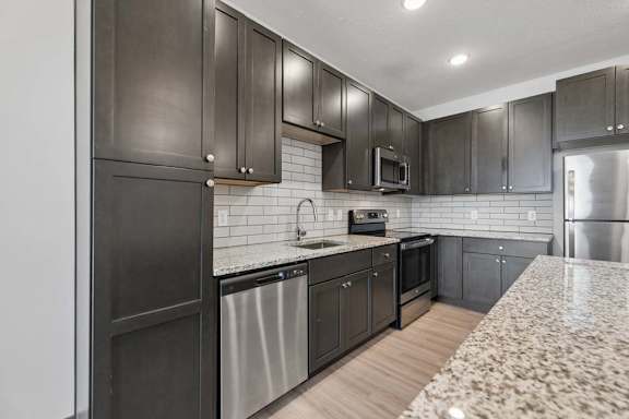 Apartment kitchen with dark cabinetry, granite countertops, subway tile backsplash, and stainless steel appliances.