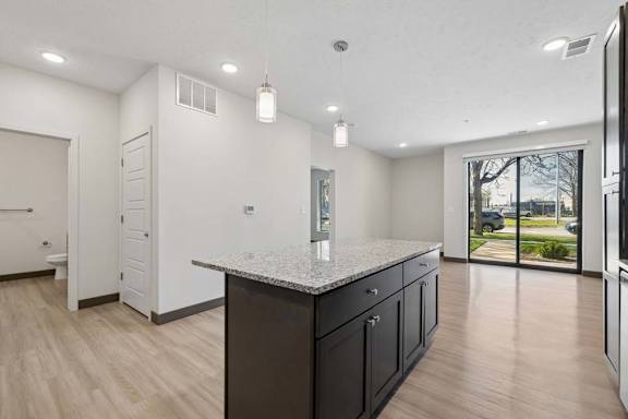 Open apartment kitchen with granite island, pendant lighting, wood-style flooring, and sliding glass doors to a patio.