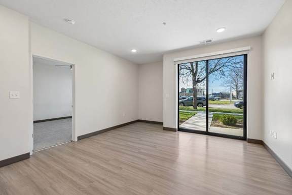Open apartment living area with wood-style flooring, recessed lighting, and sliding glass doors leading to a ground-level patio.