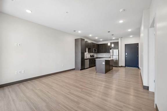 Open-concept apartment interior with wood-style flooring, recessed lighting, and a kitchen with an island and stainless steel appliances.