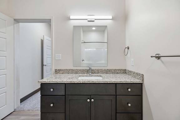 Bathroom vanity with dark cabinetry, granite countertop, undermount sink, and illuminated wall mirror.