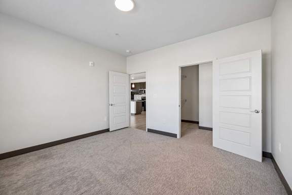 Carpeted bedroom featuring a walk-in closet and open doorway connecting to the kitchen and main living area.