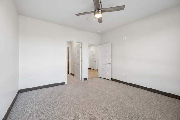 Carpeted bedroom with white walls, dark trim, a ceiling fan, and two open doorways leading to adjacent spaces.