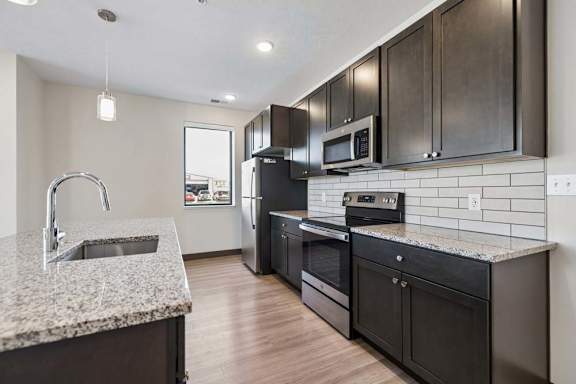 Modern kitchen with dark cabinetry, granite countertops, stainless steel appliances, and a large island with an undermount sink.